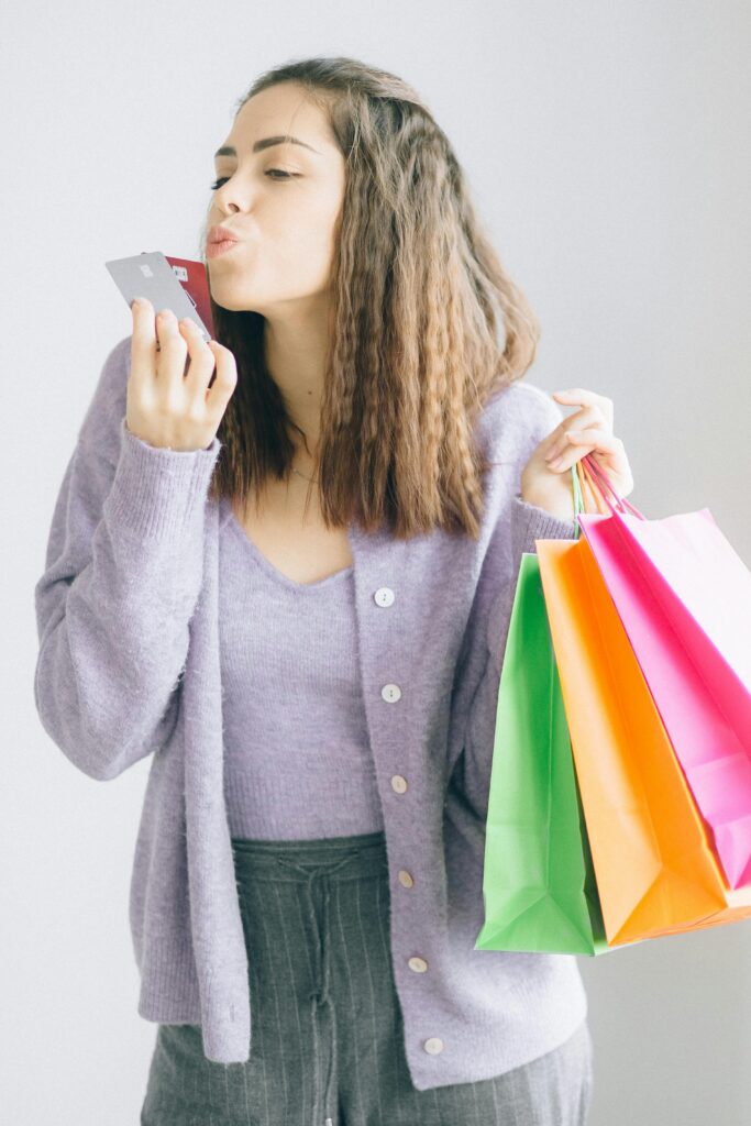 Woman playfully kissing credit card with colorful shopping bags in hand.